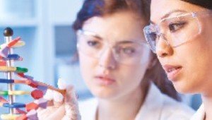 Two women wearing safety glasses examine a DNA model.