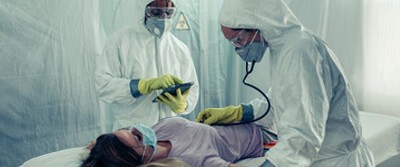 two healthcare workers tending to a patient in isolation on a gurney 